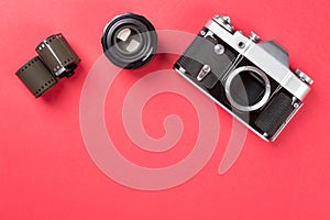 Old film camera with lens and film on red background. Top view.