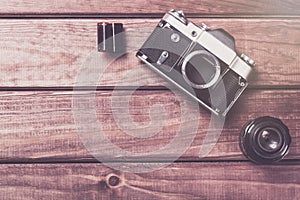 Old film camera with lens and film on wooden background. Vintage toned and top view