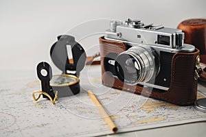 Old film photo camera, magnetic compass and pencil lying on map