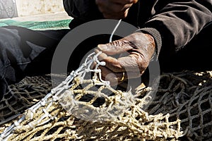 Old fisherman hand sews a fishing net