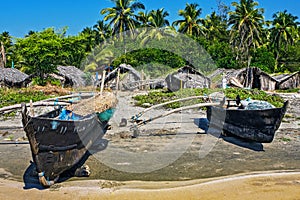 Old fishing boat on the beach in tropical with palms, huts and blue sky