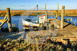 Old fishing boat moored at jetty on coastal river in marshland