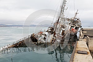 An old fishing boat sunk at a pier in seaport