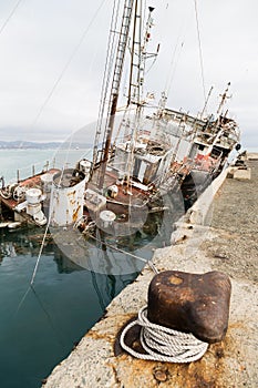 An old fishing boat sunk at a pier in seaport