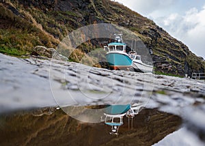 Old fishing boats in dry dock rock wall harbour moored beautiful scenery reflected in water.