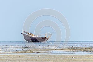 An old fishing dhow stranded at low tide in quiet shallow waters