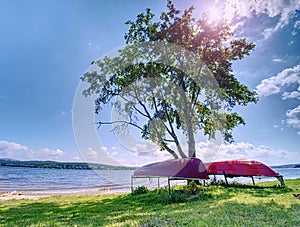 Old fishing rowing boat stacked upside down under tree at lake