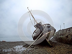 Old fishing ship at low tide on the ground. Cloudy misty day, Galway, Ireland