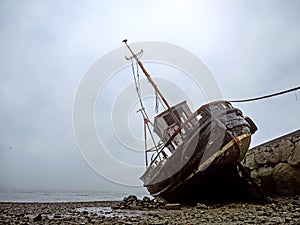 Old fishing ship at low tide on the ground. Cloudy misty day, Galway, Ireland