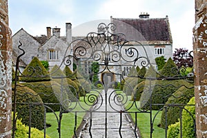 An old flag stone path leads up to an English country house viewed through a wrought iron gate. The path is bordered by elegant