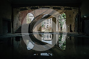 Old flooded abandoned mansion with spiral stair, water reflection