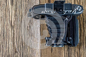 Old folding camera on a textured rustic wooden surface.