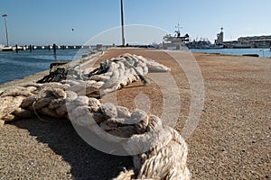 Old, frayed mooring rope lying on ground at fishing dock. Low angle