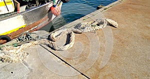 Old frayed mooring rope lying on the ground at fishing dock. Pan right.