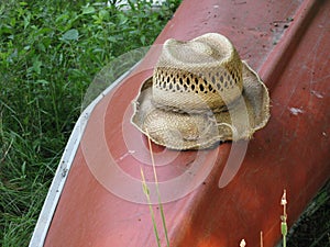 Old Frayed Straw Hat with Tattered Brim Resting on a Red Canoe After the Paddle