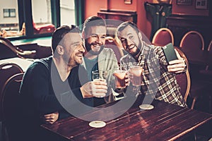 Old friends having fun taking selfie and drinking draft beer in pub.