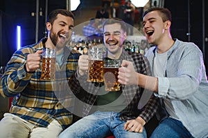 Old friends meeting. Happy young men in casual wear toasting with beer while sitting in beer pub together