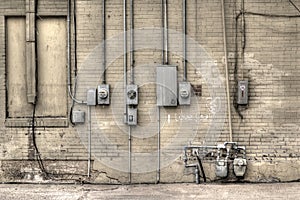 Old but functional electrical meters on yellow brick wall along a back alleyway