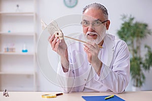 Old funny male zoology teacher demonstrating fish skeleton