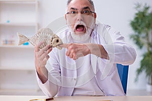 Old funny male zoology teacher demonstrating fish skeleton