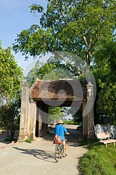 Old gate with woman cycling at Duong Lam old village, Hanoi, Vietnam