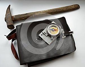 Old geological compass, a hammer and bag on gray background