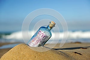 Old glass bottle with 500 euro banknote inside, sand of the beach