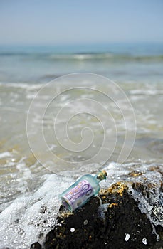 Old glass bottle with a 500 euro banknote on a rock among the waves of the sea