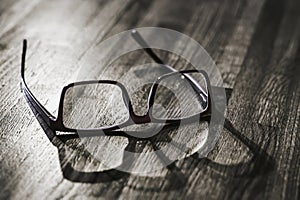 Old glasses with shadow on wooden table surface closeup