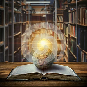 An old globe lying on an open book against the background of bookshelves in a library. Selective focus. Retro style. Science,