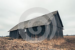 Old gloomy abandoned farm barn and yellow grass field with overcast sky.