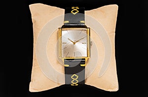 Old gold wrist watch with black handmade leather strap on black background. Retro clock with watchstrap put on beige