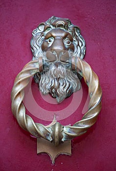 Old golden iron lion head door knocker on a wooden pink door. Mdina, Malta