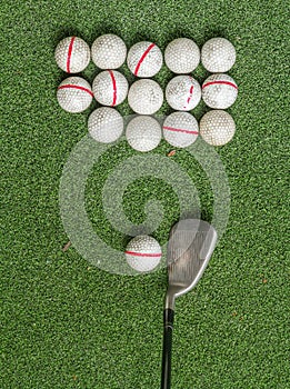 Old golf balls and iron on artificial grass in driving range.