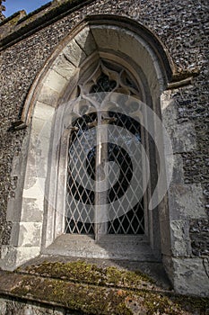 Old gothic arched carved leaded window in an old church with flint walls