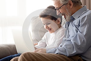 Old granddad and small grandson with laptop on couch