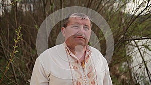 Old grandfather senior elderly man standing on the river bank in an embroidered