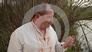 Old grandfather senior elderly man standing on the river bank in an embroidered