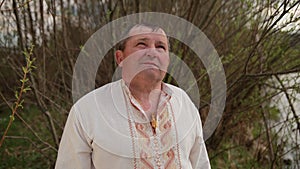 Old grandfather senior elderly man standing on the river bank in an embroidered