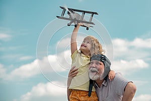 Old grandfather and young child grandson playing with toy airplane against summer sky background. Generations ages.