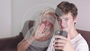 Old grandmother and adult grandson using mobile application on phone tougether seating on the sofa. Doing video call