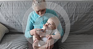 An old grandmother with gray hair and deep wrinkles holds a grandson in her arms.