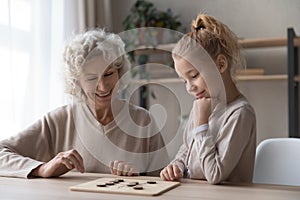 Old grandmother playing draughts with adorable little child girl.