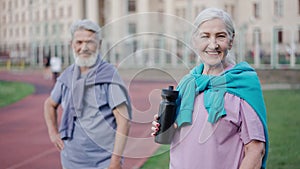 Old granny drink water from sports bottle. Elderly portrait couple look camera.