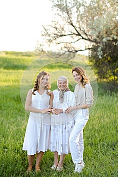 Old granny standing with adult granddaughters in white dresses.