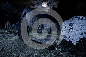 Old graveyard with ancient tombstones grave stone and old church front of full moon black raven dark night spooky horror