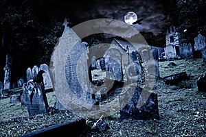 Old graveyard with ancient tombstones grave stone and old church front of full moon black raven dark night spooky horror