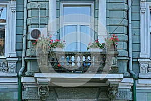 Old gray concrete balcony with window and flowerpots with red flowers