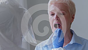 Old gray-haired woman sick elderly mature lady female patient opens mouth for pcr analysis doing covid-19 virus test