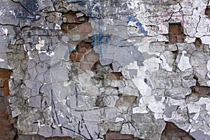 old gray heavily damaged concrete wall with deep relief and protruding red bricks, cracks and various stains of paint. rough